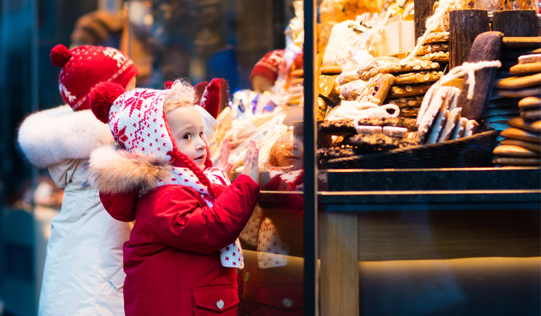 Två flickor tittar på godis och bakverk på en julmarknad.