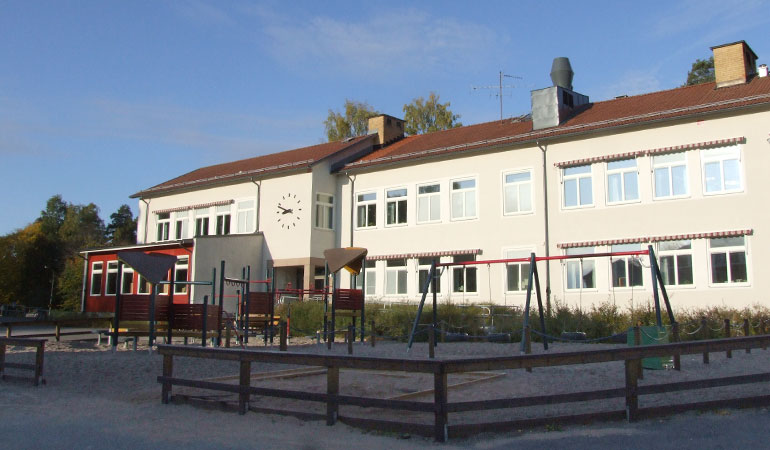 Bruksskolans skolbyggnad med lekpark i förgrunden.