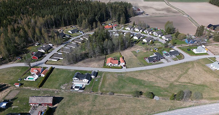 Drönarbild över aktuell tomt i Månkarbo med grönytor, hustak och gator.