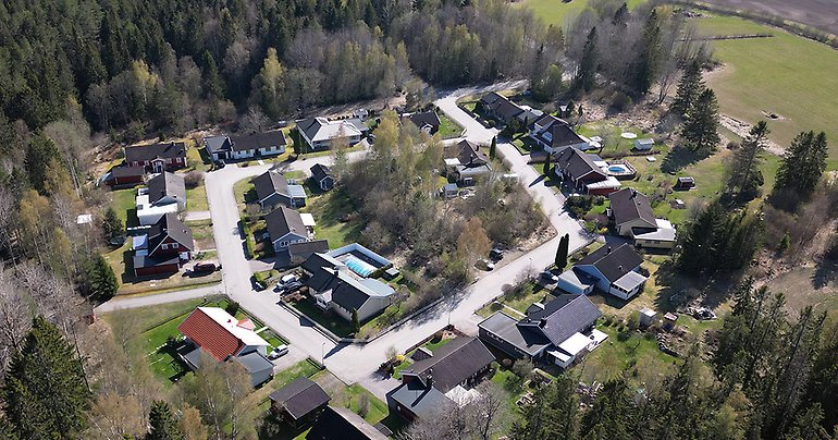Drönarbild över aktuell tomt i Karlholmsbruk med grönytor, hustak och gator.