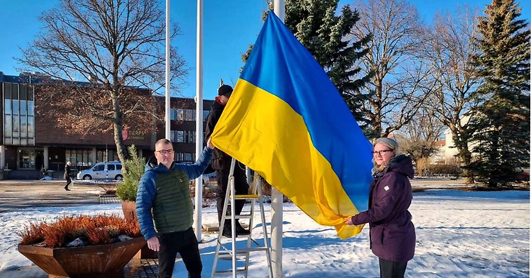 Den ukrainska flaggan hissas på torget utanför kommunhuset i Tierp. Kommunstyrelsens ordförande Sara Sjödal Centerpartiet och oppositionsrådet Jonas Nyberg Socialdemokraterna står på en varsin sida om flaggstången.